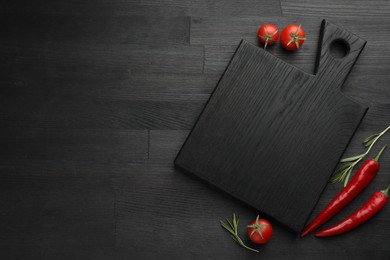 Photo of Cutting board, rosemary, chili peppers and tomatoes on black wooden table, flat lay. Space for text