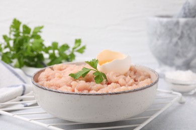 Fresh raw minced meat, parsley and egg in bowl on light grey table, closeup