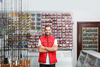 Salesman standing near showcase with fishing equipment in sports shop