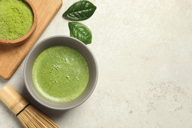 Cup of fresh matcha tea, green powder and bamboo whisk on light grey table, flat lay. Space for text