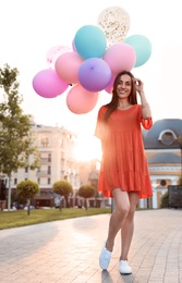 Photo of Cheerful young woman with color balloons outdoors on sunny day