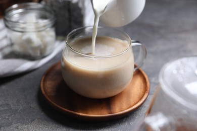 Photo of Pouring milk into cup of tea on grey table, closeup