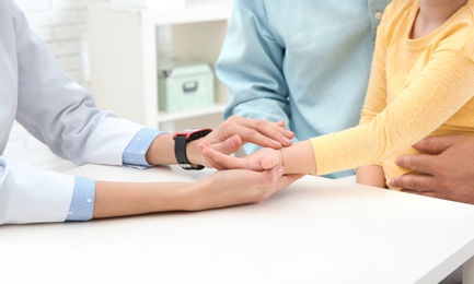 Doctor checking little girl's pulse with fingers in hospital, closeup