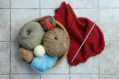 Soft woolen yarns, knitting and needles on grey tiled background, flat lay