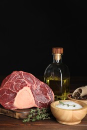 Photo of Piece of raw beef meat, thyme, oil and spices on wooden table against black background