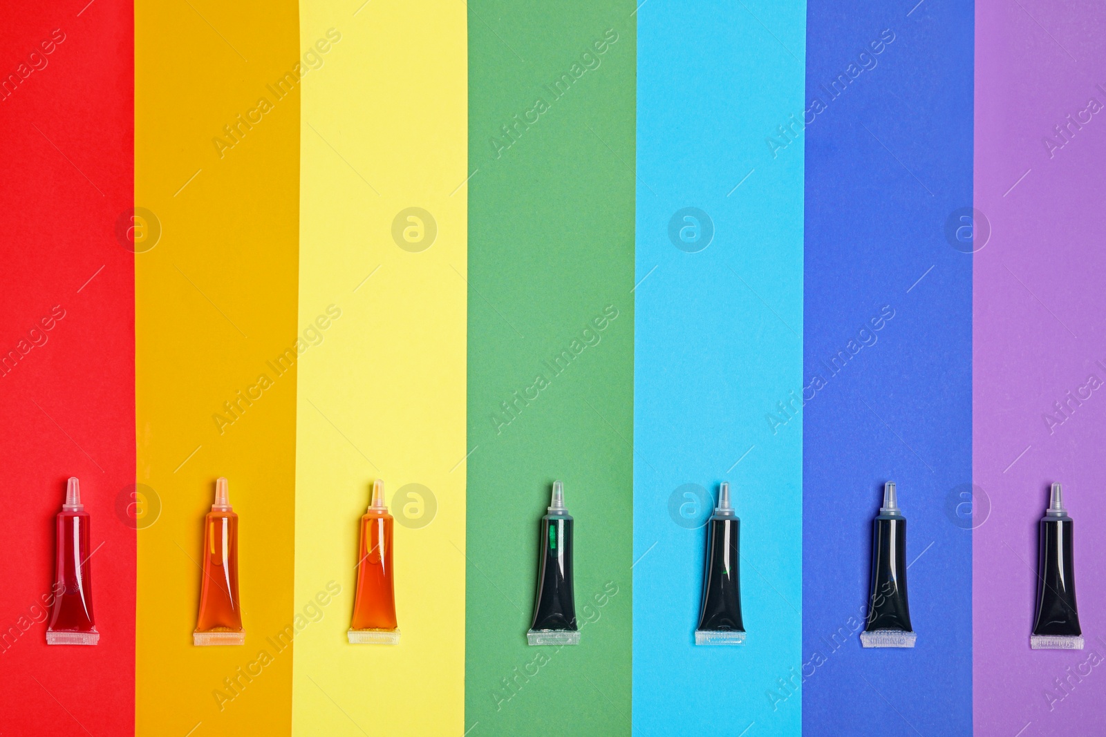 Photo of Tubes with different food coloring on rainbow background, flat lay. Space for text