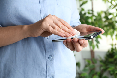 Photo of Woman cleaning smartphone with cotton pad indoors, closeup