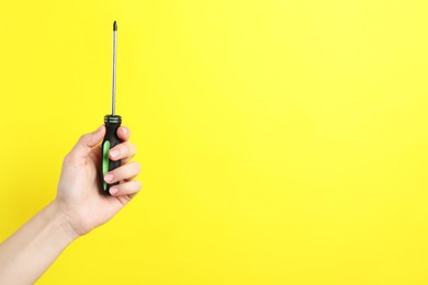 Photo of Woman holding screwdriver on yellow background, closeup. Space for text