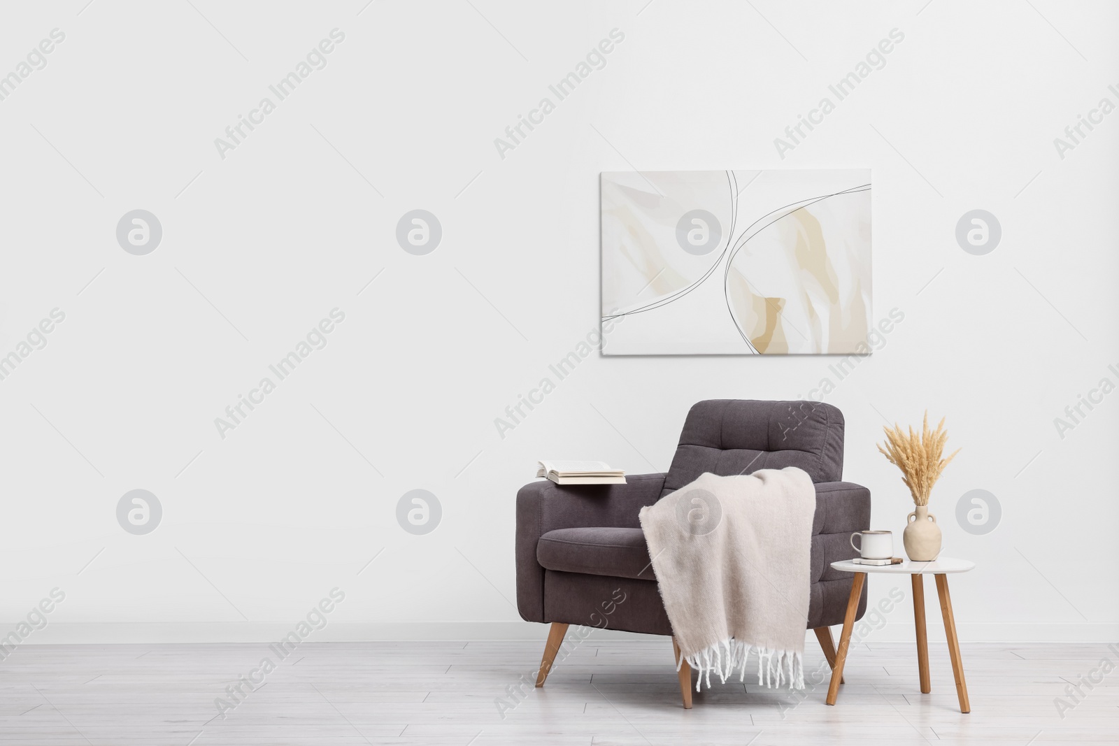 Photo of Comfortable armchair, blanket and side table near white wall indoors. Space for text