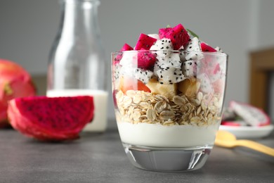 Photo of Glass of granola with different pitahayas, yogurt and other fruits on grey table, space for text