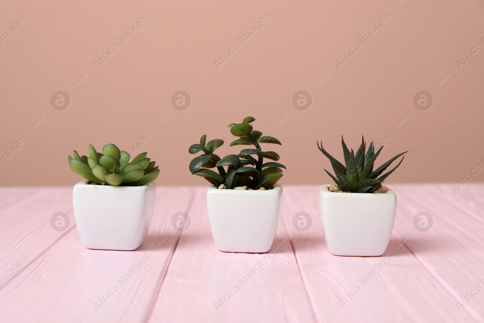 Photo of Artificial plants in white flower pots on pink wooden table