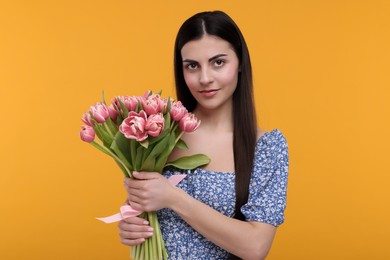 Happy young woman with beautiful bouquet on orange background