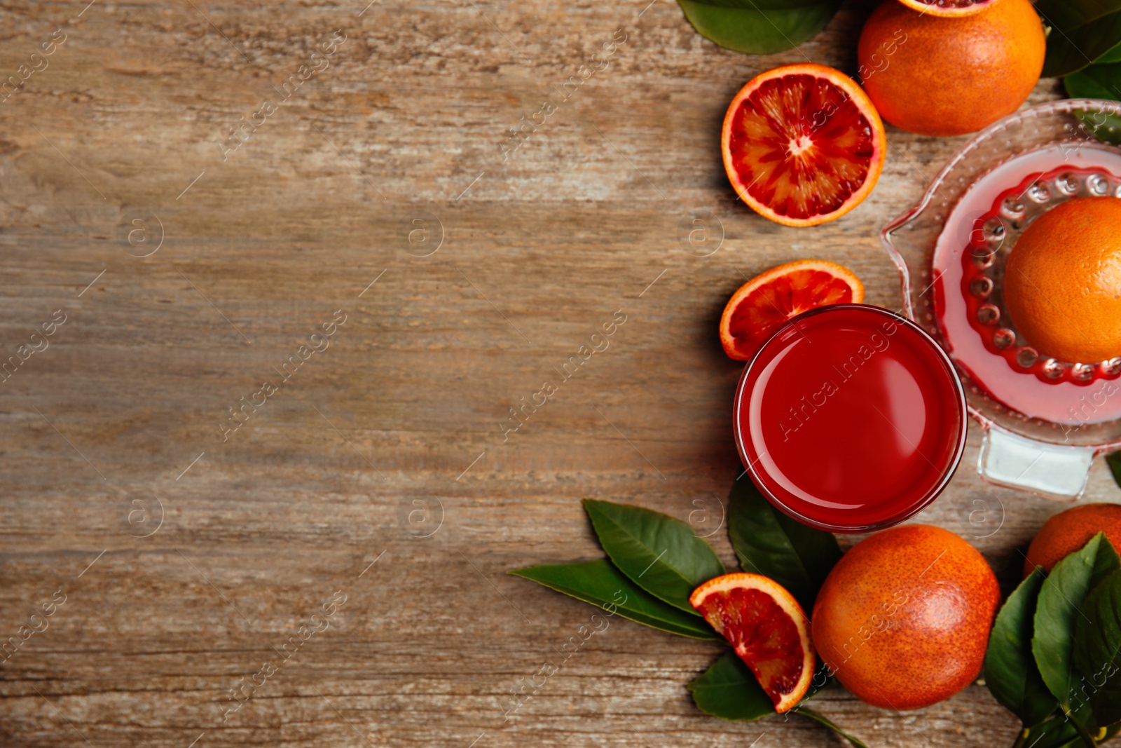 Photo of Tasty sicilian orange juice in glass, squeezer and fruits on wooden table, flat lay. Space for text