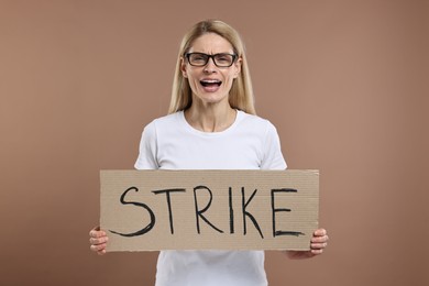 Photo of Angry woman holding cardboard banner with word Strike on brown background