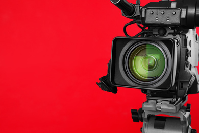 Photo of Modern professional video camera on red background, closeup. Space for text