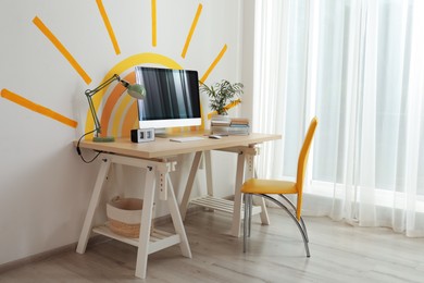 Photo of Stylish home office interior with comfortable workplace and sun art on wall