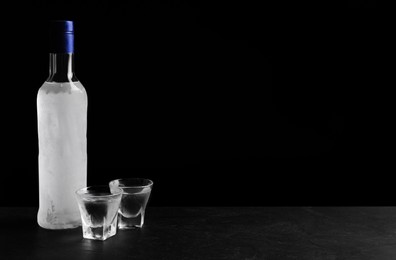 Photo of Bottle of vodka and shot glasses on table against black background. Space for text