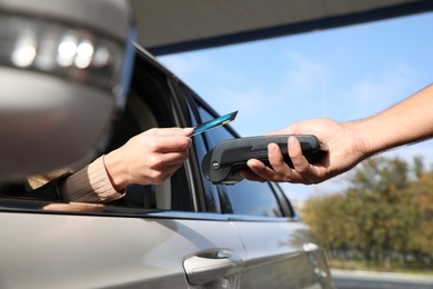 Photo of Woman sitting in car and paying with credit card at gas station, closeup