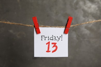 Paper note with phrase Friday! 13 hanging on twine against grey background. Bad luck superstition
