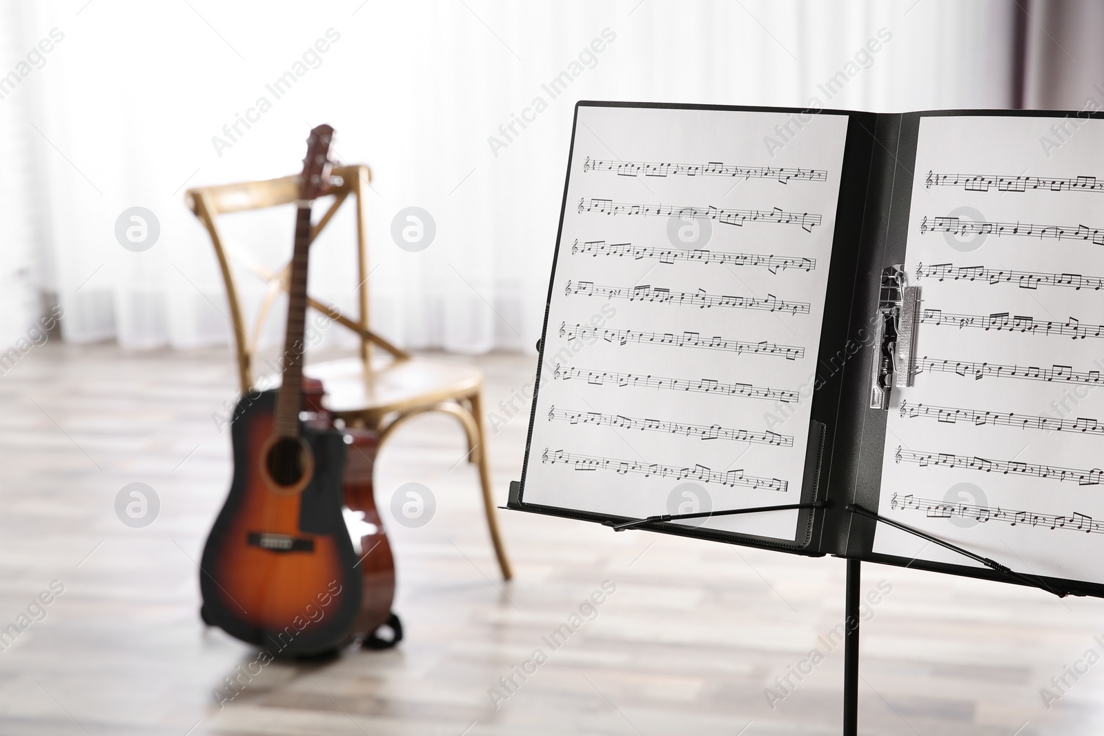 Photo of Note stand with music sheets and blurred acoustic guitar on background. Space for text