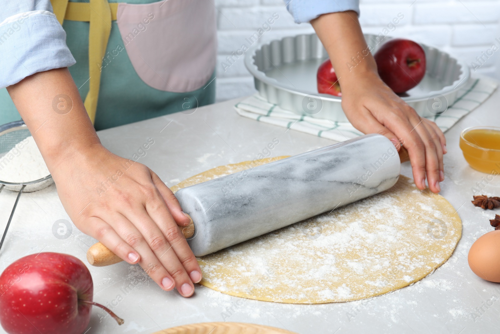 Photo of Woman rolling dough for apple pie at light grey table, closeup