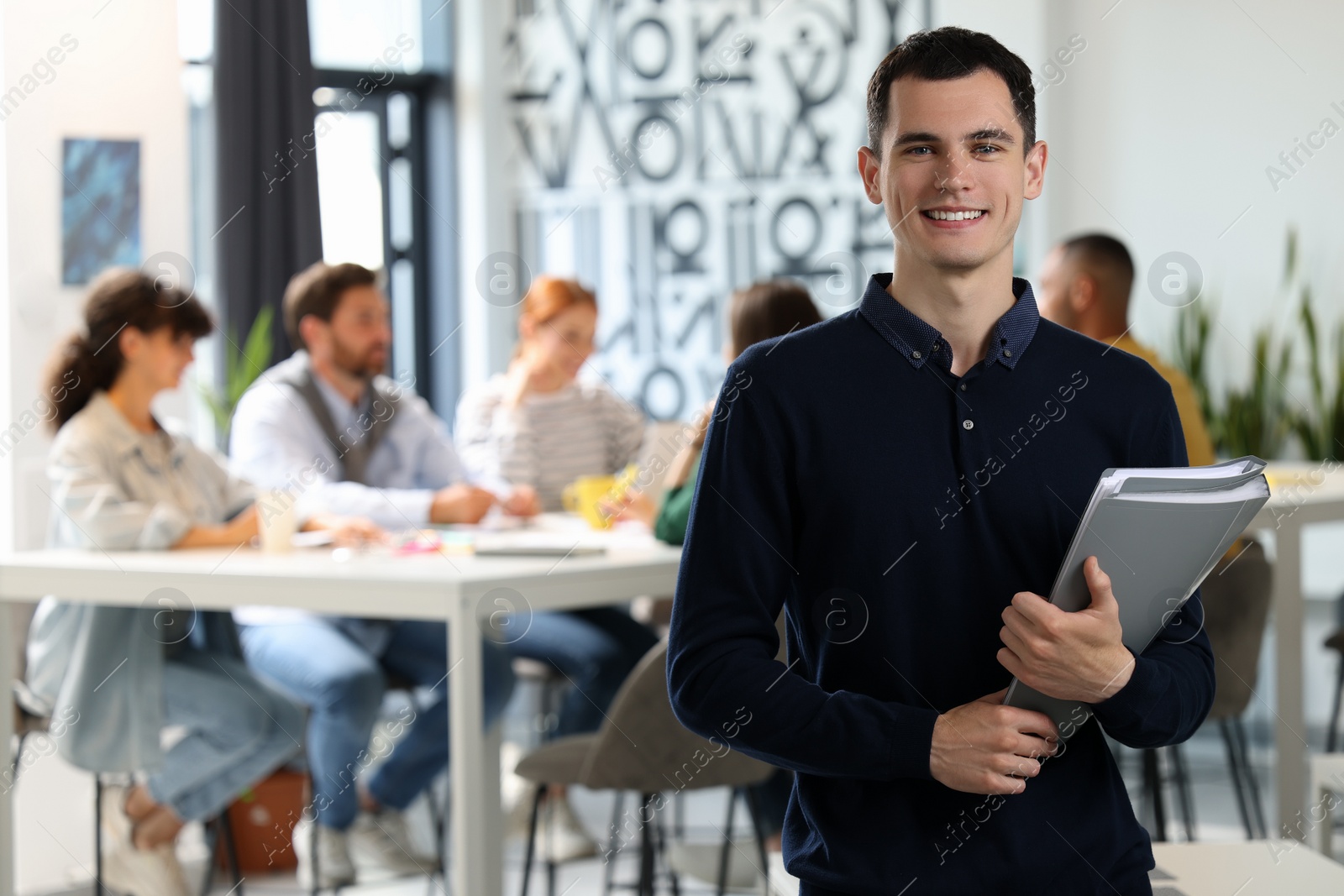 Photo of Team of employees working together in office. Happy man with folders indoors, space for text