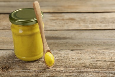 Photo of Jar and spoon with tasty mustard sauce on wooden table, space for text