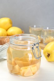 Photo of Delicious quince drink in glass jar and fresh fruits on white wooden table