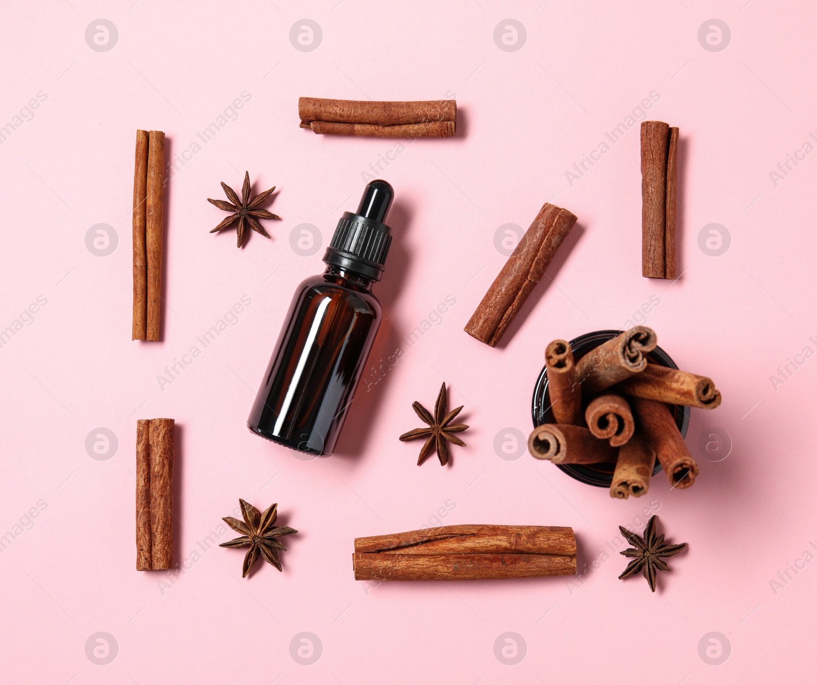 Photo of Flat lay composition with bottle of essential oil and cinnamon sticks on pink background