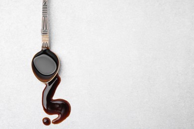 Photo of Spoon with balsamic vinegar on white table, top view. Space for text