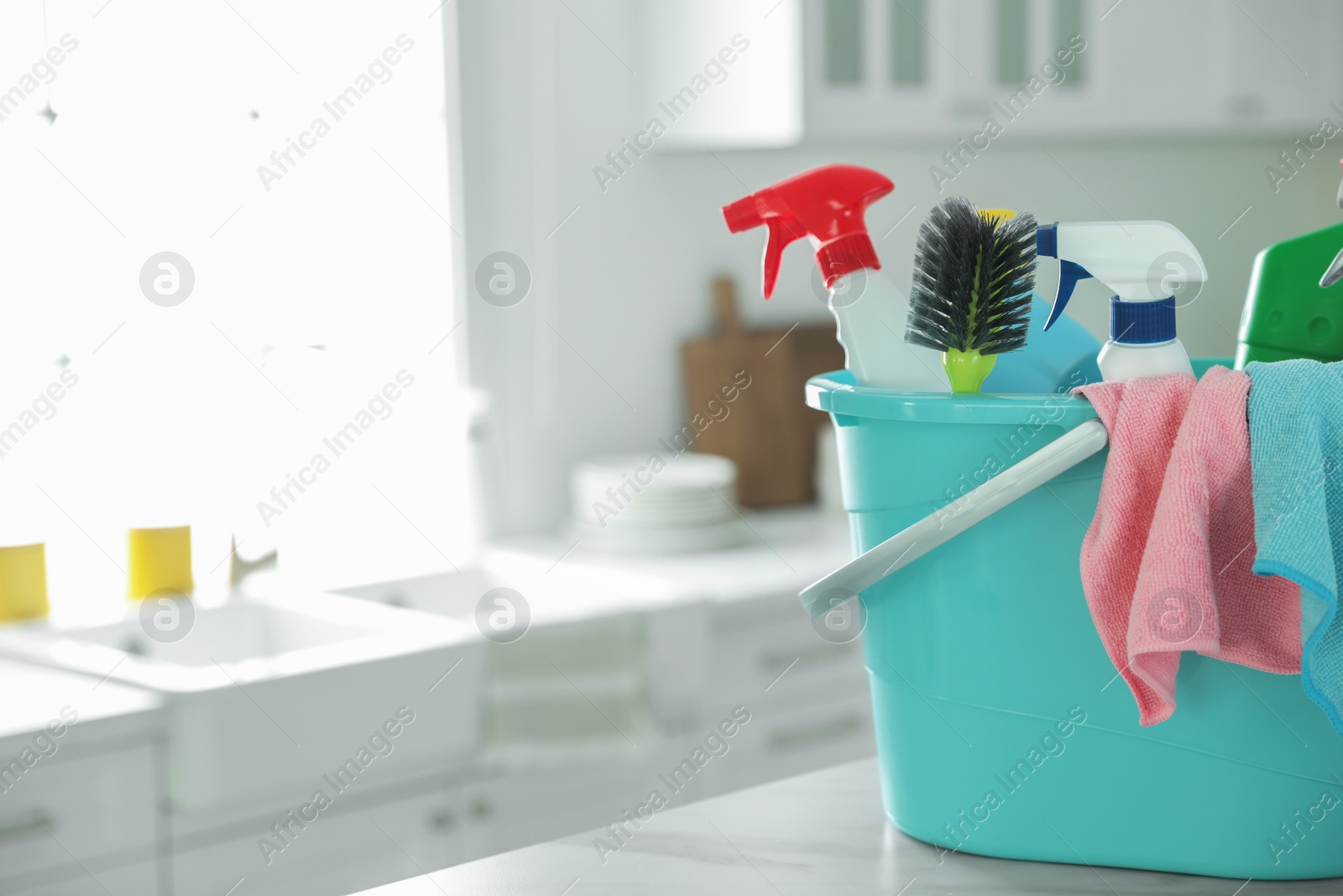 Photo of Plastic bucket with different cleaning supplies on table in kitchen. Space for text