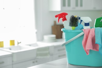 Plastic bucket with different cleaning supplies on table in kitchen. Space for text