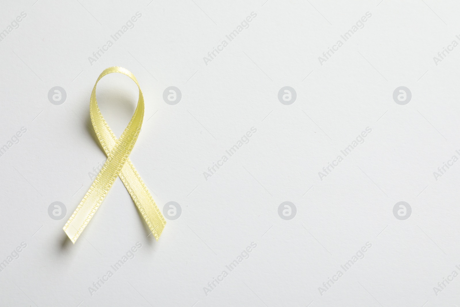 Photo of Yellow ribbon on white background, top view. Cancer awareness