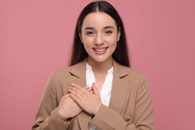 Photo of Thank you gesture. Beautiful grateful woman with hands on chest against pink background