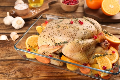 Raw chicken, orange slices and other ingredients i baking dish on wooden table