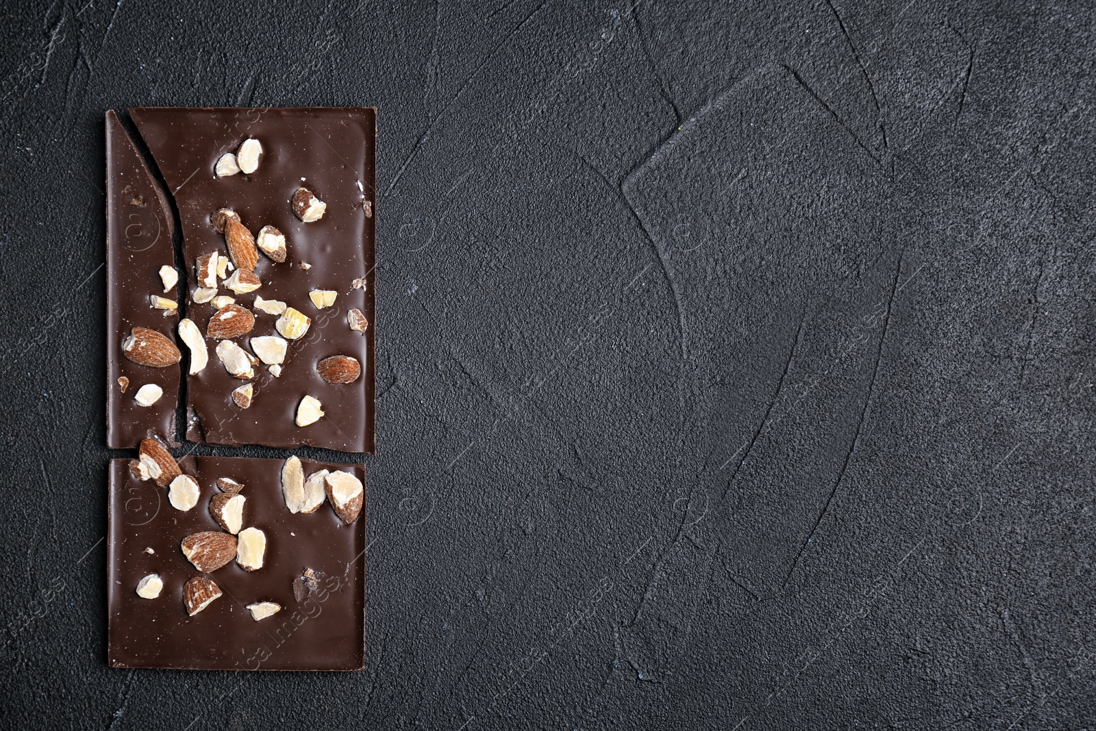 Photo of Delicious chocolate bar with nuts on dark table, top view