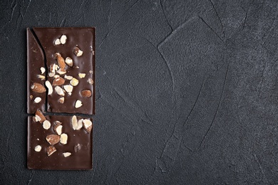 Photo of Delicious chocolate bar with nuts on dark table, top view