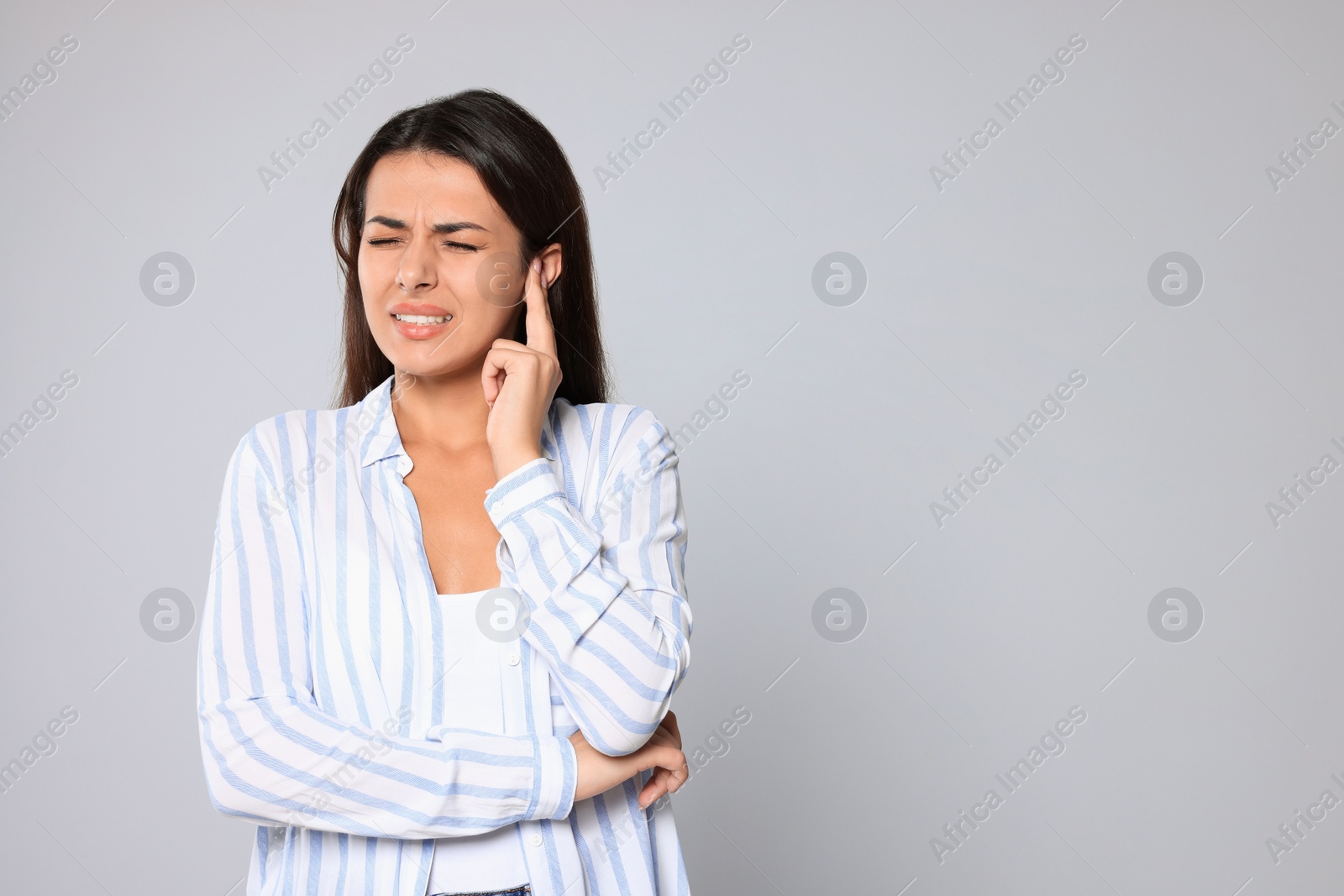Photo of Young woman suffering from ear pain on light grey background, space for text