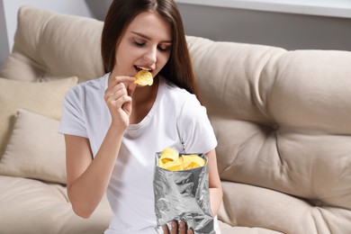 Photo of Pretty young woman eating tasty potato chips on sofa at home