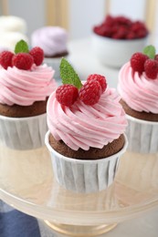 Photo of Delicious cupcakes with cream and raspberries on stand