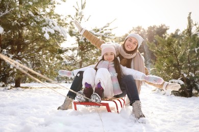 Happy mother and daughter sledding outdoors on winter day. Christmas vacation