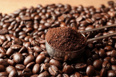 Spoon with coffee grounds and roasted beans on table, closeup