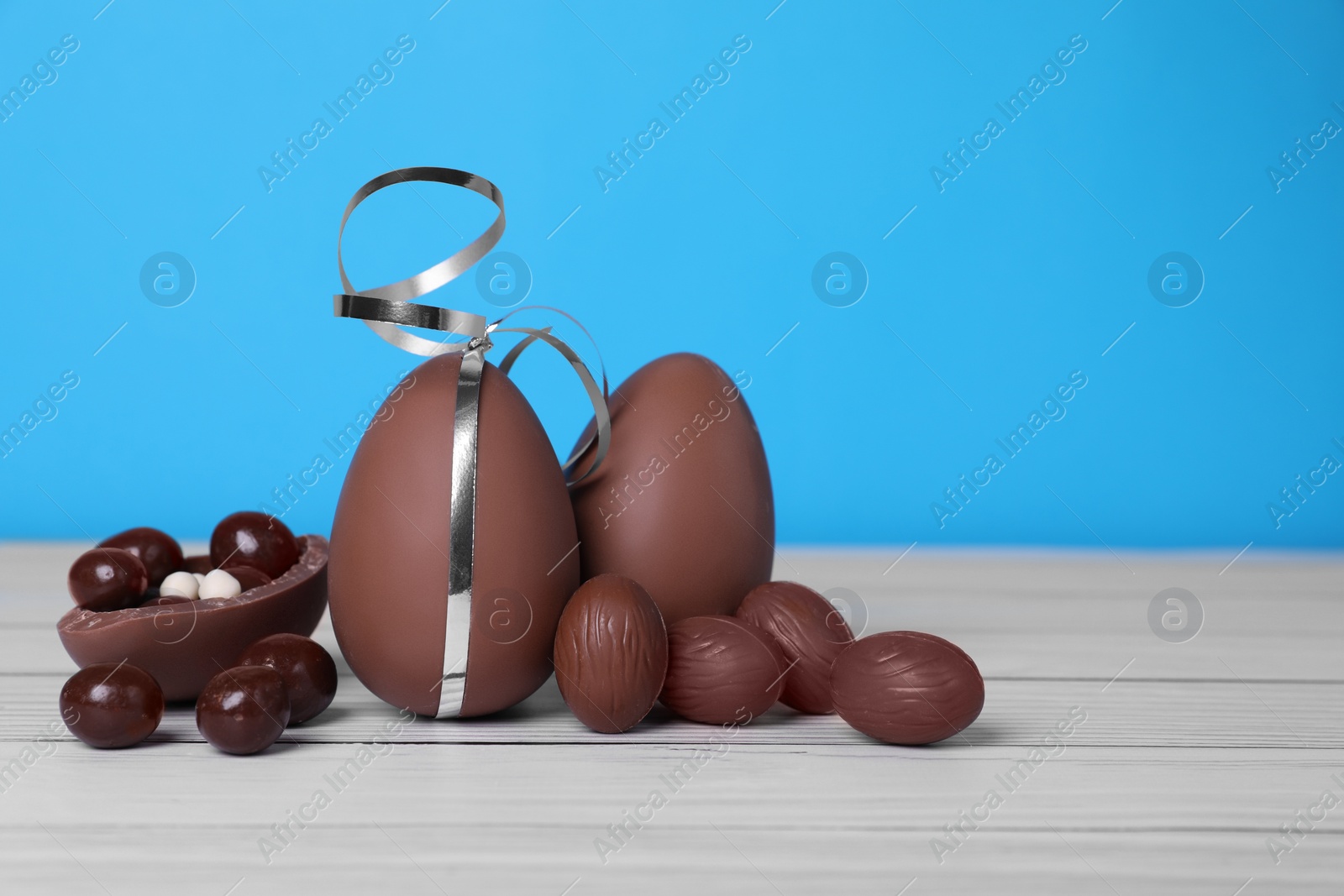 Photo of Delicious chocolate eggs and candies on white wooden table against light blue background. Space for text