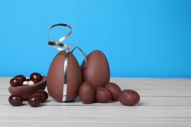 Photo of Delicious chocolate eggs and candies on white wooden table against light blue background. Space for text