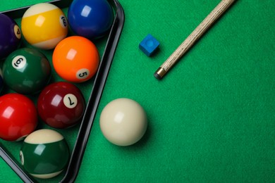 Photo of Set of billiard balls with rack, cue and chalk on green table, flat lay. Space for text
