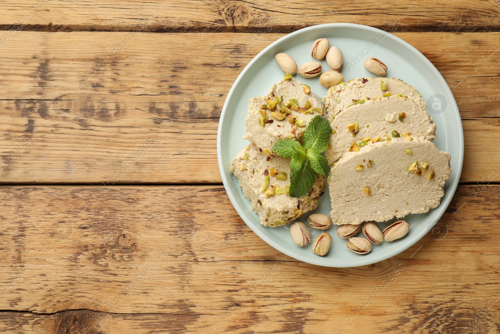 Photo of Tasty halva with pistachios and mint on wooden table, top view. Space for text