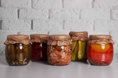 Photo of Many glass jars with different preserved vegetables on light grey table