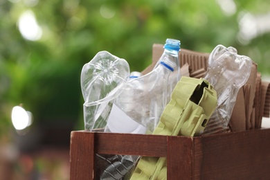 Photo of Wooden crate with different garbage on blurred background, closeup. Waste recycling concept