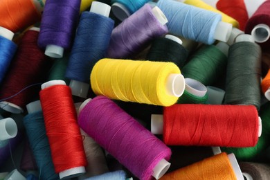 Photo of Pile of colorful sewing threads as background, closeup