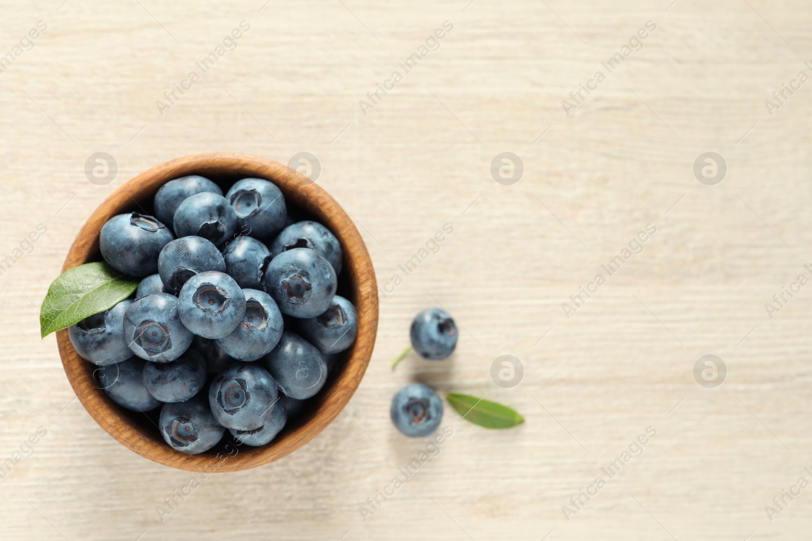 Photo of Bowl of fresh tasty blueberries on white wooden table, flat lay. Space for text